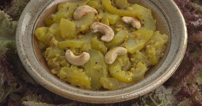 Torai ki sabzi - homemade Pakistani-style zucchini curry decorated with roasted cashew nuts in a bowl on a lettuce leaf background.