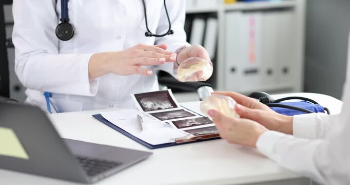 Plastic surgeon shows silicone chest implants to woman in clinic. Breast augmentation and lift concept