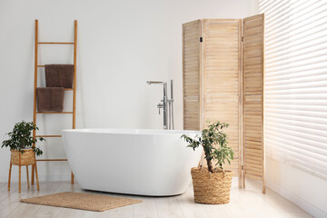 Wooden folding screen, bathtub and green houseplants in bathroom