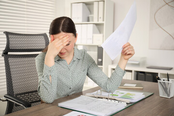 Embarrassed woman with document at wooden table in office
