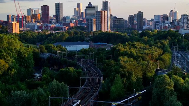 Aerial view of Manchester skyline at sunset with greenery in foreground and trams passing