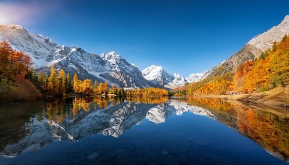Obraz premium A picturesque alpine lake surrounded by snow-capped mountains, with the lake’s surface perfectly reflecting the vibrant colors of the autumn foliage.