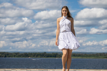 Young beautiful girl in a summer dress walking along the embankment