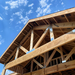 Obraz premium New home build with exposed rafters and framing is framed against a bright blue sky with white clouds