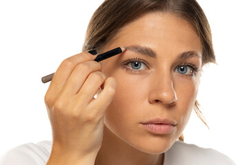 Fototapeta premium Eyebrow care up close. Cute young woman doing eyebrow styling with pencil on a white background