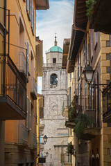 Fototapeta premium Ein malerischer Blick auf den Glockenturm der Basilika San Giacomo in Bellagio, Italien, eingerahmt von engen Straßen und bunten Gebäuden.