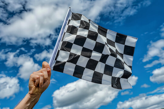 A checkered race flag held in hand against a clear blue sky, symbolizing victory and excitement in motorsport event