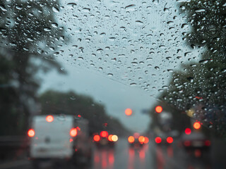 Closeup of rain drops on a windshield, and blurry road traffic with cars and red and orange lights....