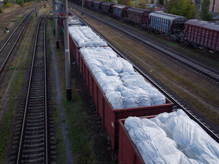 A long goods freight train with wagons without roofs loaded with huge white sacks and waiting at...