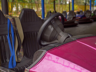Closeup of a wheel and two seats of an electric old-fashioned bumper car and a row of autos...