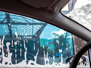 Car soaking under thick fluffy foam at a self-serve car wash. View from inside of the driver's...