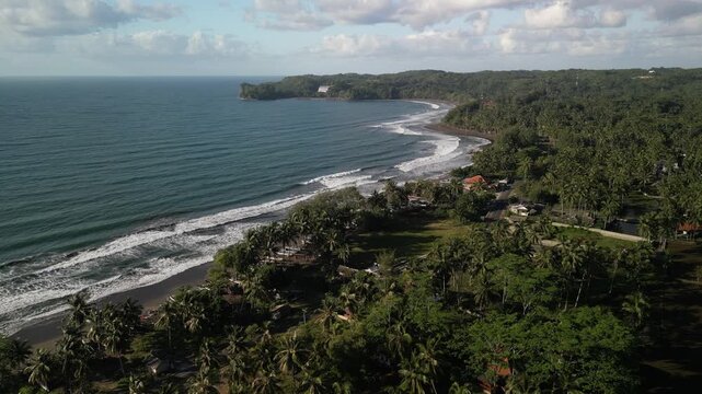 Drone flies over the traditional rice fields with coconut palm trees and move towards the sea. Paddy plantation located near the beach in Batukaras, Pangandaran, West Java Indonesia.