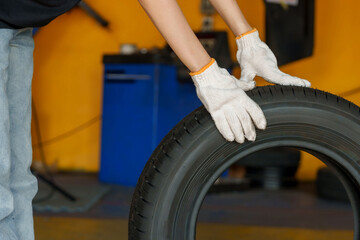 Mechanic's gloved hands rolling a tire in auto repair shop. manual labor, teamwork, and hands-on work in automotive maintenance. Represents precision, skill, physical work involved in tire handling