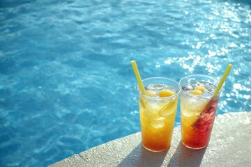Two glasses iced tea edge swimming pool are Two colorful drinks
