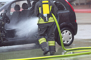 firefighter with mask and oxygen tank spraying extinguishing foam on the damaged car