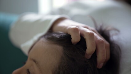 Close-up of a child’s head, with a parent's hand gently stroking the child's hair, showcasing a...