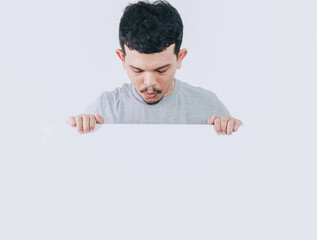 shocked expression of asian man looking down while holding banner blank signboard or copyspace for...