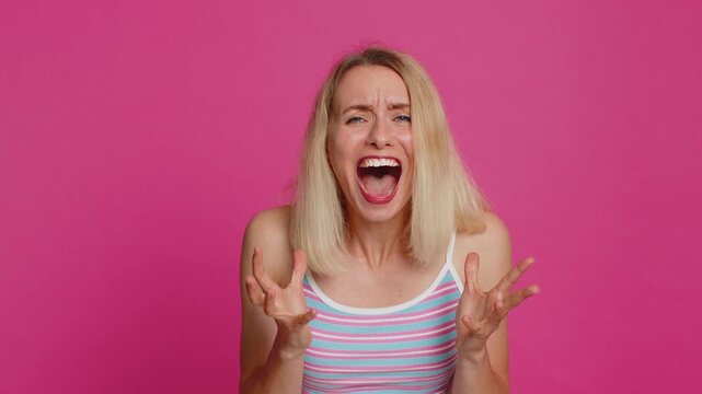 Irritated angry Caucasian young woman 30 years old screams from stress tension problems feels horror hopelessness fear surprise shock expresses rage nervous, quarrel. Girl isolated on pink background