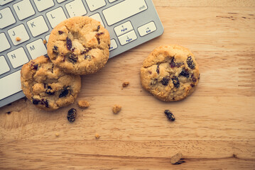 Flat lay of white chocolate chip cookies on keyboard computer on wooden table background copy...