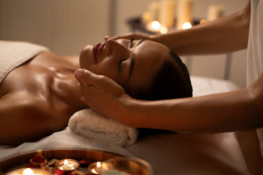 Relaxed young woman having face massage at romantic atmosphere in spa salon. Face building concept