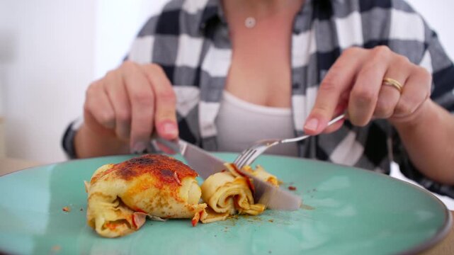 Person in checkered shirt cutting into a serving of homemade enchiladas on a green plate, ready to enjoy a tasty meal