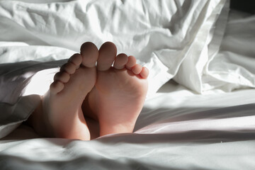 Child feet under the white blanket under soft morning light