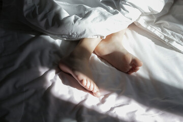Child feet under the white blanket under soft morning light