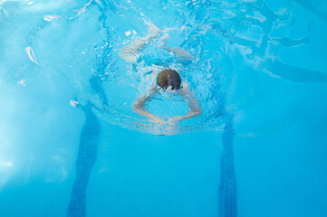 Caucasian 11 years old kid in motion swimming breaststroke in a swimming pool in summer having fun and exercising. Enjoying healthy and funny life concept. Horizontal photography with copy space.