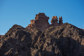The rugged beauty of a desert landscape is captured as the sun casts its glow on sandstone spires, which stand proudly against a clear, pale sky.