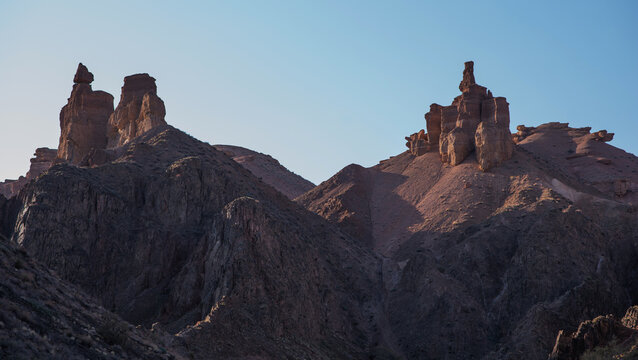 The rugged beauty of a desert landscape is captured as the sun casts its glow on sandstone spires, which stand proudly against a clear, pale sky.