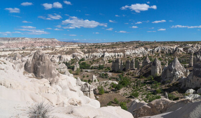 A serene landscape with the iconic fairy chimneys of Cappadocia, Turkey, under a vibrant blue sky dotted with fluffy clouds, showcasing nature's sculpture in the form of wind-swept rock formations.