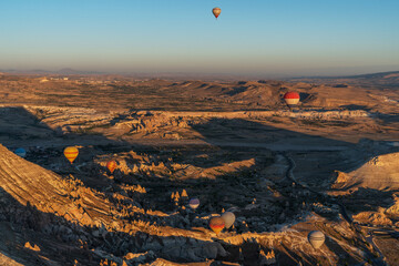 Naklejka premium multiple hot air balloons rise above a stark landscape of eroded rock formations, casting colorful silhouettes against the clear sky.