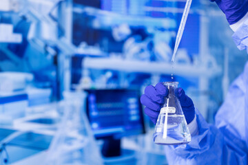 A scientist is holding a beaker filled with a clear liquid. Concept of precision and focus, as the scientist carefully handles the beaker