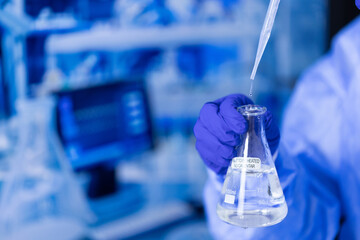A scientist is holding a beaker filled with a clear liquid. The beaker is labeled with the number 1000