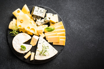 Cheese platter with craft cheese assortment on slate board at black background. Top view with copy...