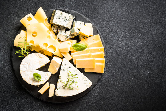 Cheese platter with craft cheese assortment on slate board at black background. Top view with copy space.