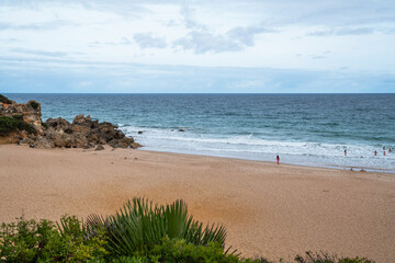 A secluded sandy beach bordered by rugged cliffs and Mediterranean shrubbery, with a solitary...