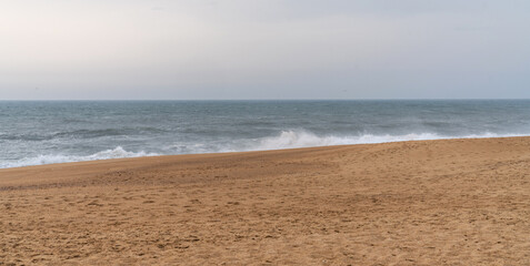 Overlooking a quiet beach with golden sands that meet rolling waves under a somber sky. Powerful waves cresting towards the sandy shore offering a sense of calm and solitude.