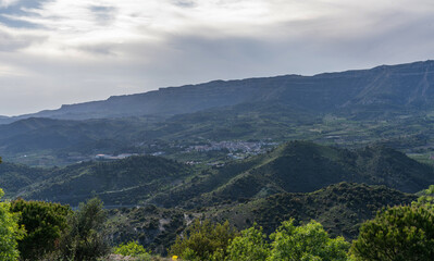 A verdant valley nestled between layered mountain escarpments under a hazy sky, with patches of cultivated land painting a mosaic of agriculture.