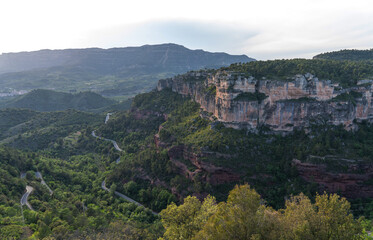 Fototapeta premium breathtaking view of majestic cliffs with layered rock formations, winding roads through lush greenery, and a serene skyline at dusk.