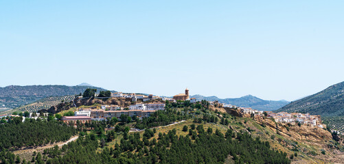 Obraz premium a quaint hilltop village with buildings perched along the ridge, surrounded by lush vegetation and rolling hills under a clear blue sky