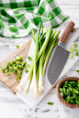Marble cutting board with cut fresh green onions on wooden white table