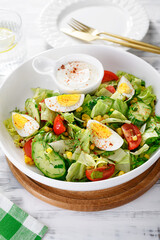 Healthy green summer salad with boiled egg, cucumber and corn.