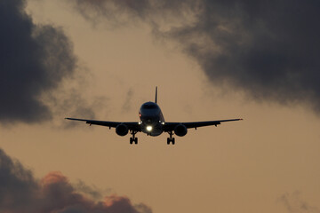 Airplane flying in the blue sky with clouds at sunset time.