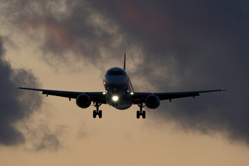 Airplane flying in the blue sky with clouds at sunset time.