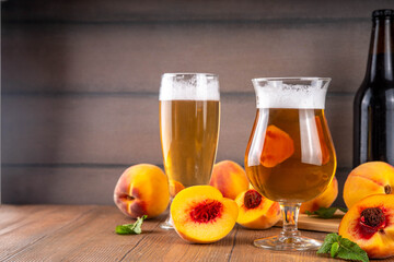 Glasses with Sour Sweet fruit Peach Craft Beer or Ale on wooden table with fresh peach slices
