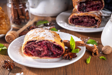 Homemade fragrant autumn cherry strudel with raisins, nuts, honey, cinnamon spices, on plate on kitchen table copy space 
