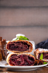 Homemade fragrant autumn cherry strudel with raisins, nuts, honey, cinnamon spices, on plate on kitchen table copy space 