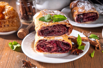 Homemade fragrant autumn cherry strudel with raisins, nuts, honey, cinnamon spices, on plate on kitchen table copy space 