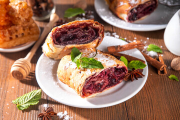 Homemade fragrant autumn cherry strudel with raisins, nuts, honey, cinnamon spices, on plate on kitchen table copy space 